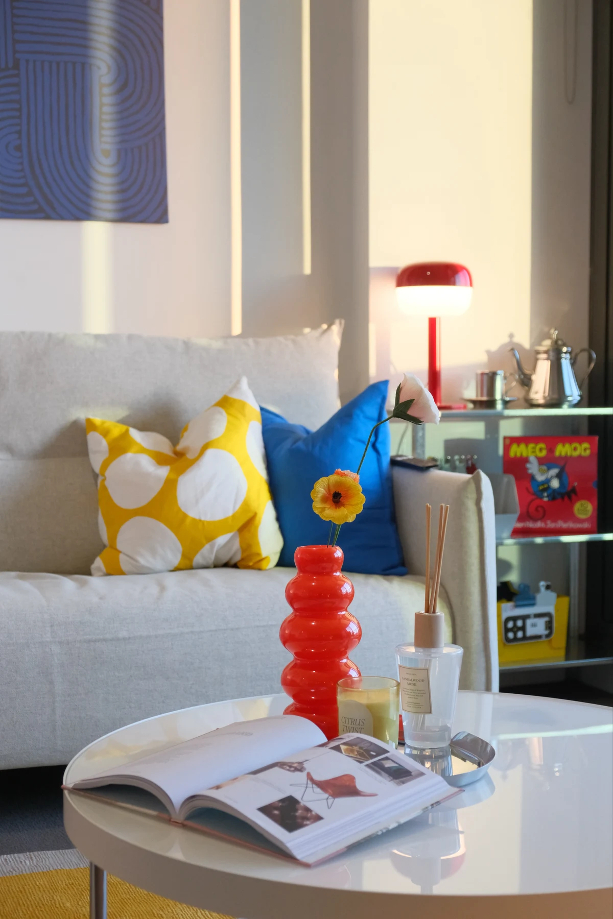 Sunlit living room with blue and yellow cushions and a red vase